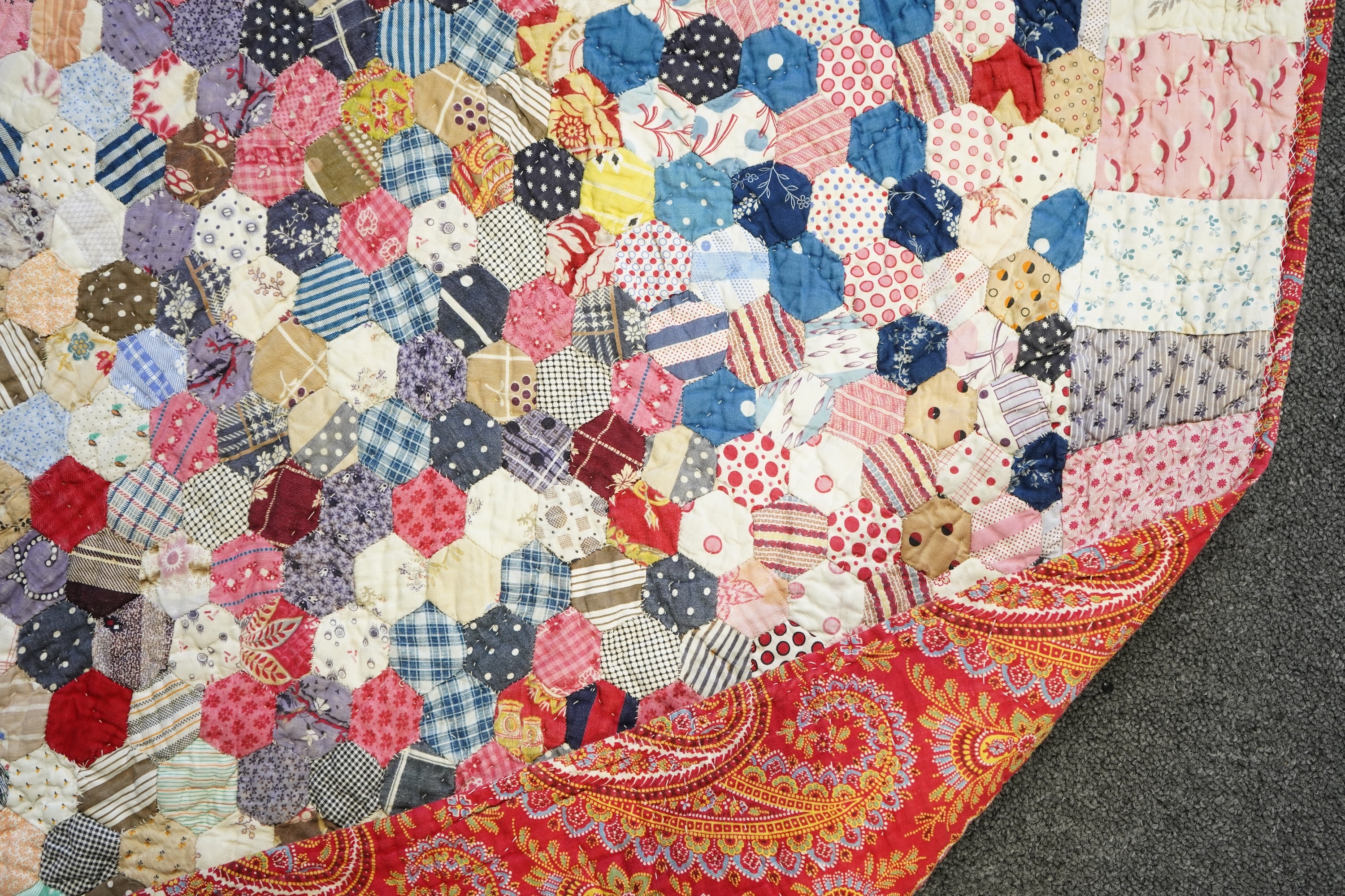 An English cotton hexagon hand made and hand pieced quilt, made from a large variety of printed dress fabrics from 19th century. The quilt edged with a wide stripped multi fabric border. The under side designed in wide s